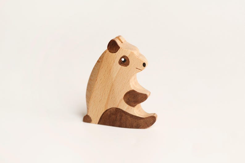 Puede incluir: Una figura de panda de madera clara con detalles en marr&oacute;n oscuro en las orejas, los parches de los ojos, las extremidades y la base. La figura del animal est&aacute; representada en posici&oacute;n sentada con un acabado liso y veta de madera visible.