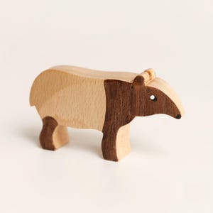 Puede incluir: Una figura de tapir de madera hecha con dos tonos de madera distintos. El cuerpo presenta una secci&oacute;n de color beige claro en la parte trasera y una secci&oacute;n de color marr&oacute;n oscuro que cubre la parte delantera, la cabeza y las patas.