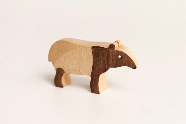Puede incluir: Una figura de tapir de madera hecha con dos tonos de madera distintos. El cuerpo presenta una secci&oacute;n de color beige claro en la parte trasera y una secci&oacute;n de color marr&oacute;n oscuro que cubre la parte delantera, la cabeza y las patas.