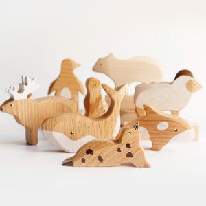 May include: A set of wooden animal figurines, including a reindeer, penguin, whale, seal, bear, sheep, and a bird. The figurines are painted in natural wood tones with white accents.