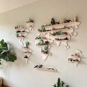 Może przedstawiać: Drewniana półka ścienna w kształcie mapy świata, niepomalowana z czarnymi konturami, prezentująca miniaturowe figurki zwierząt i drzew. Półki są wypełnione kolorowymi figurkami. Mapa jest zamontowana na jasnozielonej ścianie.