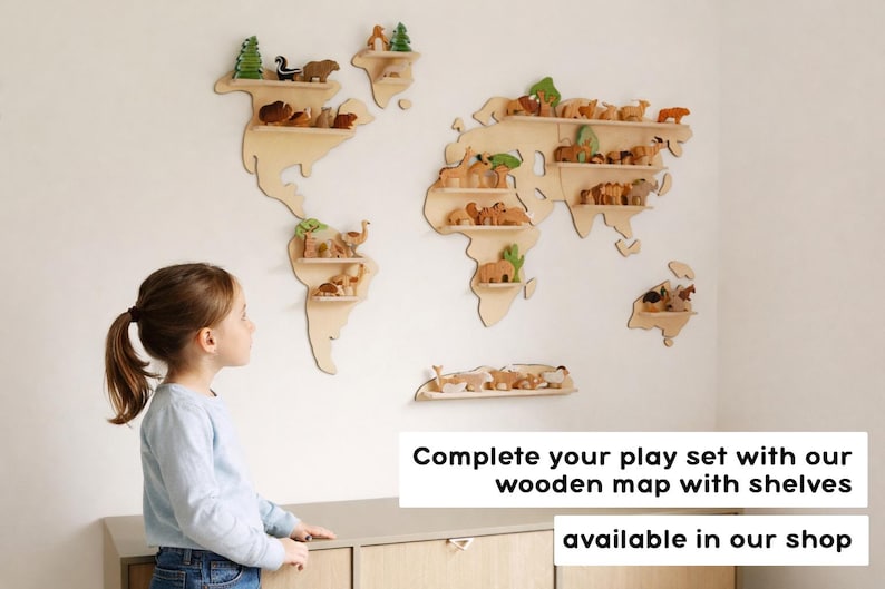 Puede incluir: Un mapa del mundo de madera de color claro para pared con estantes horizontales integrados. El mapa est&aacute; decorado con varias figuras peque&ntilde;as de madera de animales y &aacute;rboles. El texto en la imagen dice: Complete your play set with our wooden map with shelves available in our shop.