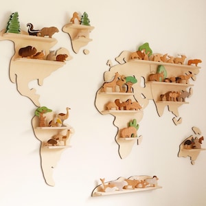 May include: Wooden world map shelves, each holding wooden animal figurines and trees. The shelves are mounted on a white wall, creating a decorative and educational display for a child's room or nursery.