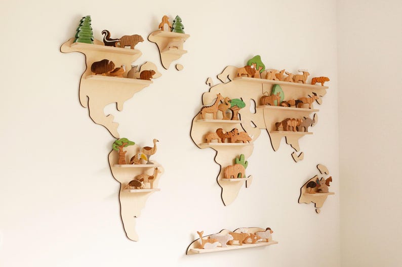 May include: Wooden world map shelves, each holding wooden animal figurines and trees. The shelves are mounted on a white wall, creating a decorative and educational display for a child's room or nursery.