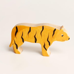 Puede incluir: Una figura de tigre de madera con cuerpo amarillo y rayas verticales negras pintadas. La figura animal se muestra en posici&oacute;n de perfil de pie con un acabado liso, exhibiendo una forma tallada sencilla con detalles de oreja y ojo.