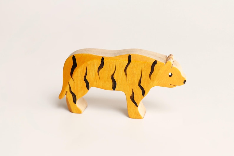 Puede incluir: Una figura de tigre de madera con cuerpo amarillo y rayas verticales negras pintadas. La figura animal se muestra en posici&oacute;n de perfil de pie con un acabado liso, exhibiendo una forma tallada sencilla con detalles de oreja y ojo.