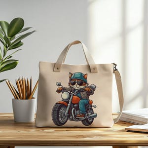 May include: A beige canvas tote bag with a graphic of a cat wearing sunglasses and a helmet riding a motorcycle. The cat is wearing a blue jacket and jeans.