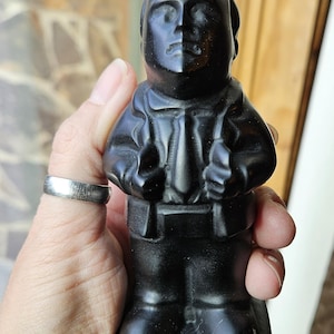 May include: Black ceramic figurine of a person wearing a jacket and tie. The figurine is standing on a square base.