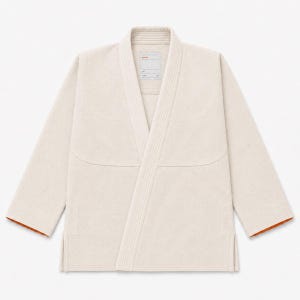 May include: A beige kimono-style jacket with long sleeves, a thick reinforced collar, and side slits. The interior lining is a contrasting orange color. A rectangular label is stitched at the inner neckline with the text "paa" in orange.