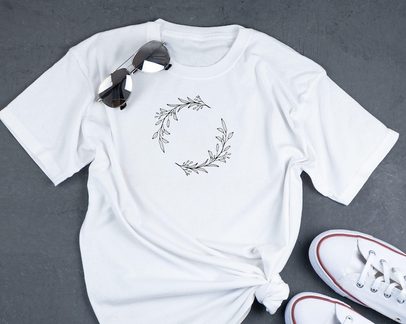 Puede incluir: Camiseta blanca con un dise&ntilde;o simple de corona de flores negra.