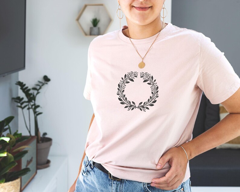 Puede incluir: Una camiseta rosa con un dise&ntilde;o de corona de flores negra.