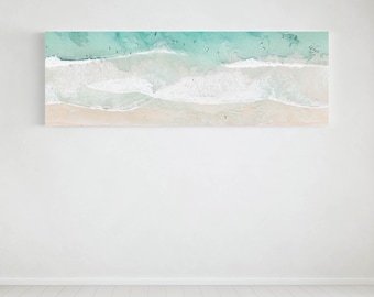 May include: A rectangular canvas print of a beach scene. The image shows an aerial view of the ocean with turquoise water, white waves, and a sandy beach. Small figures of people are visible in the water and on the sand.