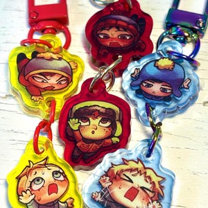 May include: A collection of six acrylic keychains featuring cartoon character illustrations. Each charm is attached to a colorful metal lobster clasp, including red, yellow, and iridescent finishes. The characters are depicted in various expressive poses.