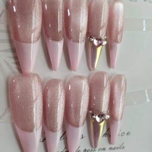 May include: Set of ten artificial nails in a light pink color with a glittery top section and a French tip design. Two nails feature a gold-colored accent with rhinestones. The text "your choice is the best choice" is visible.
