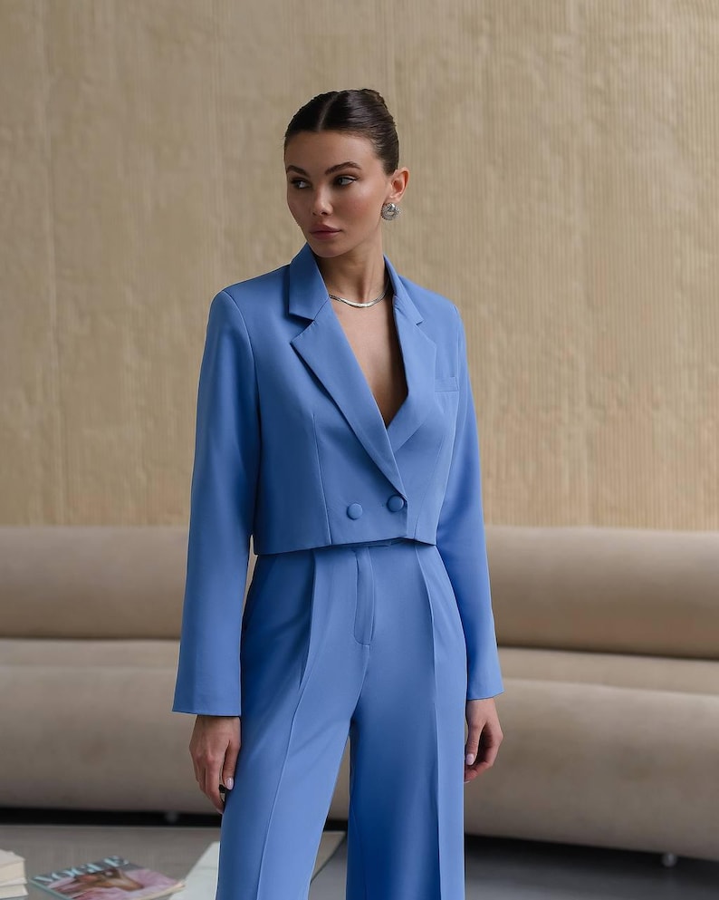 K&ouml;nnte beinhalten: Ein blauer, kurzer Blazer mit doppelreihigem Verschluss und langen &Auml;rmeln. Der Blazer wird mit einer passenden weiten Hose kombiniert.