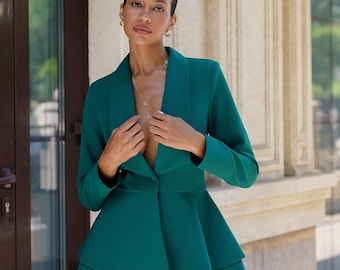 May include: A teal green blazer with a ruffled hem and a deep V-neckline. The blazer is worn over a matching pair of pants.