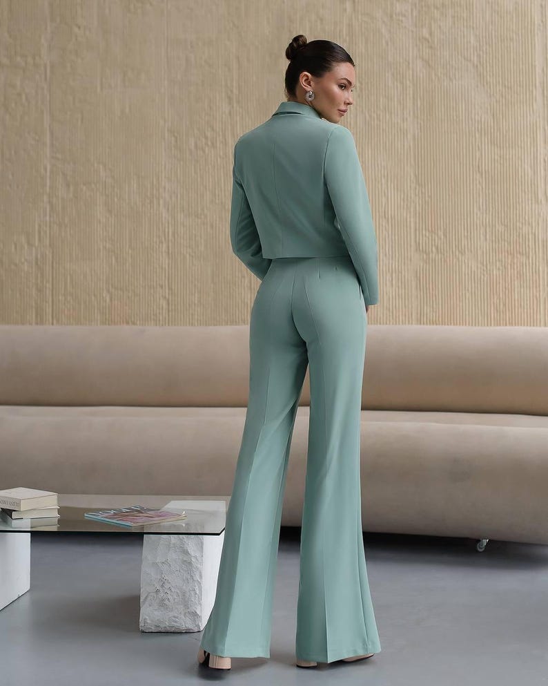 K&ouml;nnte beinhalten: Ein hellgr&uuml;ner, kurzer Blazer und eine passende weite Hose. Der Blazer hat einen zweireihigen Verschluss und einen Schalkragen.