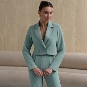 K&ouml;nnte beinhalten: Ein mintgr&uuml;ner, kurzer Blazer mit doppelreihigem Verschluss und dazu passende weite Hose. Der Blazer hat eine G&uuml;rtelschlaufe und die Hose einen hohen Bund.