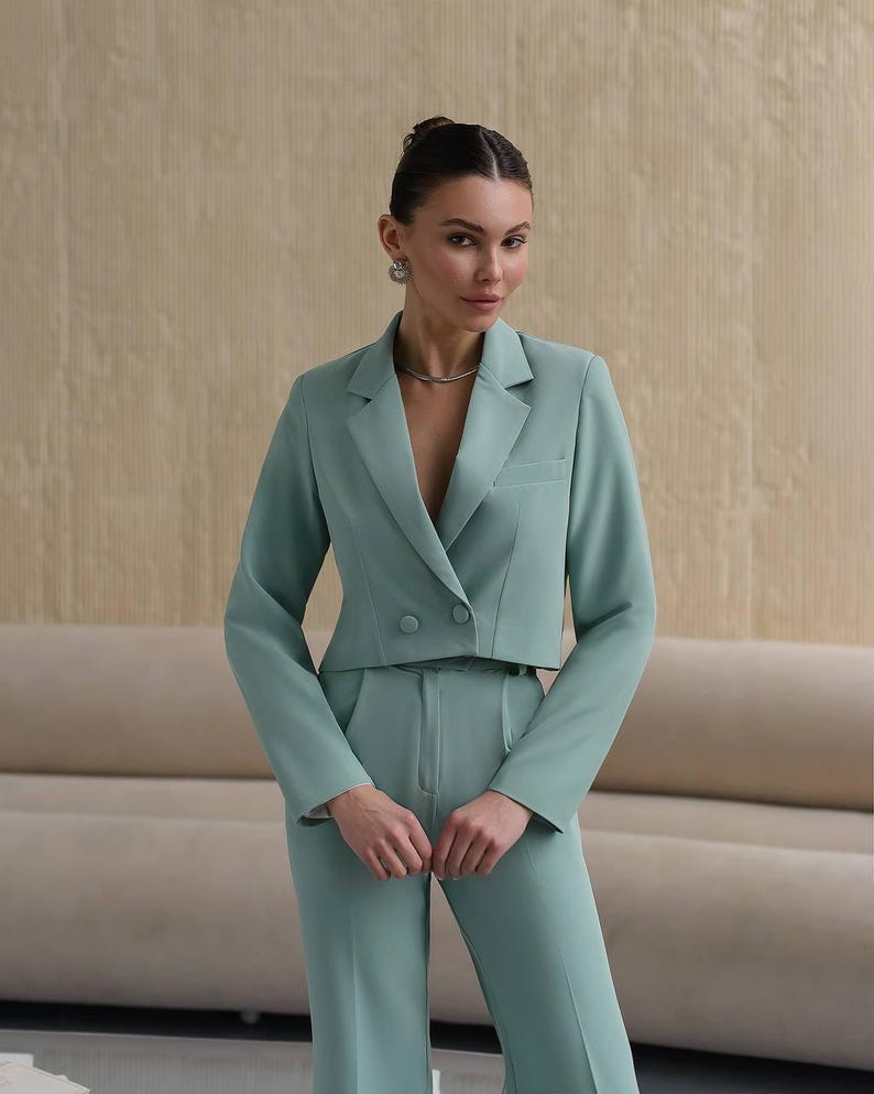 K&ouml;nnte beinhalten: Ein mintgr&uuml;ner, kurzer Blazer mit doppelreihigem Verschluss und dazu passende weite Hose. Der Blazer hat eine G&uuml;rtelschlaufe und die Hose einen hohen Bund.