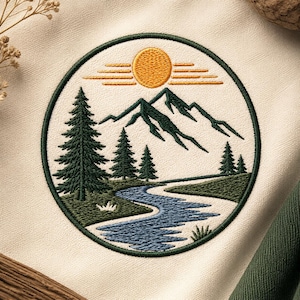 Op de afbeelding: Een ronde geborduurde patch op crèmekleurige stof met een landschapsscène met een gele zon, donkergroene bergtoppen, naaldbomen en een kronkelende blauwe rivier. Het ontwerp is omsloten door een donkergroene cirkelvormige randsteek.