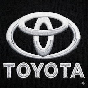 Könnte beinhalten: Gesticktes weißes Toyota-Logo und -Text auf schwarzem Hintergrund. Das Logo ist ein stilisierter Oval mit sich überlappenden Formen. Das Wort "TOYOTA" ist darunter in passendem weißem Faden gestickt.