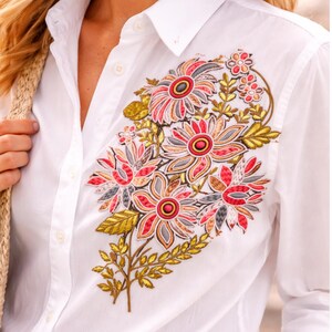 Puede incluir: Camisa blanca con diseño floral bordado. El bordado presenta flores rojas, rosas, grises y amarillas con hojas verdes. La camisa tiene cuello clásico y puños abotonados.