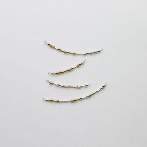 May include: Four curved jewelry components with small gold and silver beads strung on wire. Each piece has a small loop at each end. The beads are arranged in a pattern, with some sections of gold and silver beads.