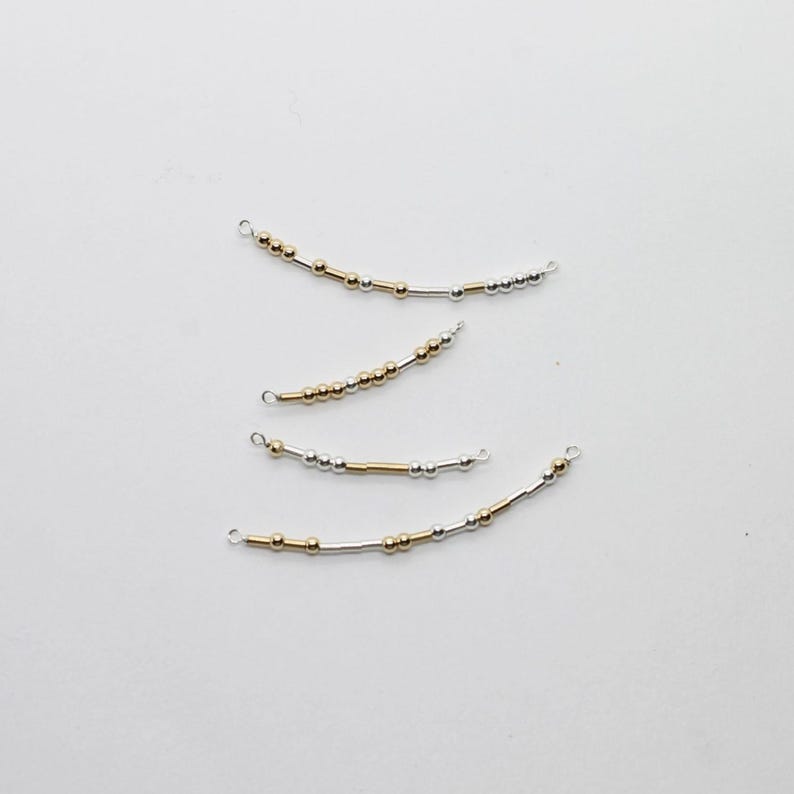 May include: Four curved jewelry components with small gold and silver beads strung on wire. Each piece has a small loop at each end. The beads are arranged in a pattern, with some sections of gold and silver beads.