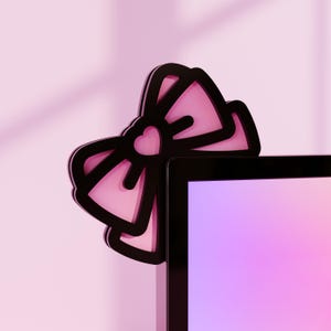 Peut inclure: Un nœud rose et noir avec un cœur au centre est attaché à un écran d'ordinateur noir.