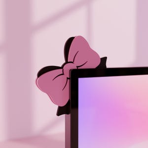 Peut inclure: Décoration d'angle d'écran d'ordinateur en forme de nœud papillon rose et noir. Le nœud papillon est rose clair avec un centre noir et est fixé au coin d'un écran d'ordinateur noir. Le fond est rose clair.