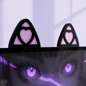 Peut inclure: Décorations d'écran d'ordinateur en forme d'oreilles de chat noires avec un motif de cœur rose. Les oreilles sont montées sur le dessus d'un écran d'ordinateur, avec un gros plan d'une illustration numérique des yeux d'une femme visible à l'écran.