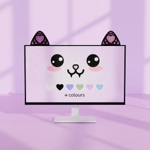 Peut inclure: Un écran d'ordinateur rose affichant un visage de chat de dessin animé avec des yeux noirs, des joues roses et un nez noir. Le moniteur a des oreilles de chat sur le dessus et une sélection d'options de couleur en forme de cœur en dessous. Le texte "+ couleurs" est également affiché.