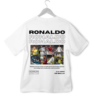 May include: White t-shirt with a collage of photos of Cristiano Ronaldo, a soccer player, and the text "RONALDO" repeated three times. The text "LA VIDA ES BELLA" is also included on the shirt. The quote "Siempre crei que no hay un limite para lo que puedes alcanzar. Con trabajo duro y dedicaci&oacute;n, todo es posible." is printed on the shirt.