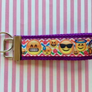 May include: Purple key chain with a silver key ring and a colourful ribbon with emoji faces.