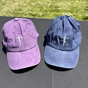 May include: Two baseball caps with a distressed look. One is purple and the other is blue. Both have a white cross with the word "faith" written on it.