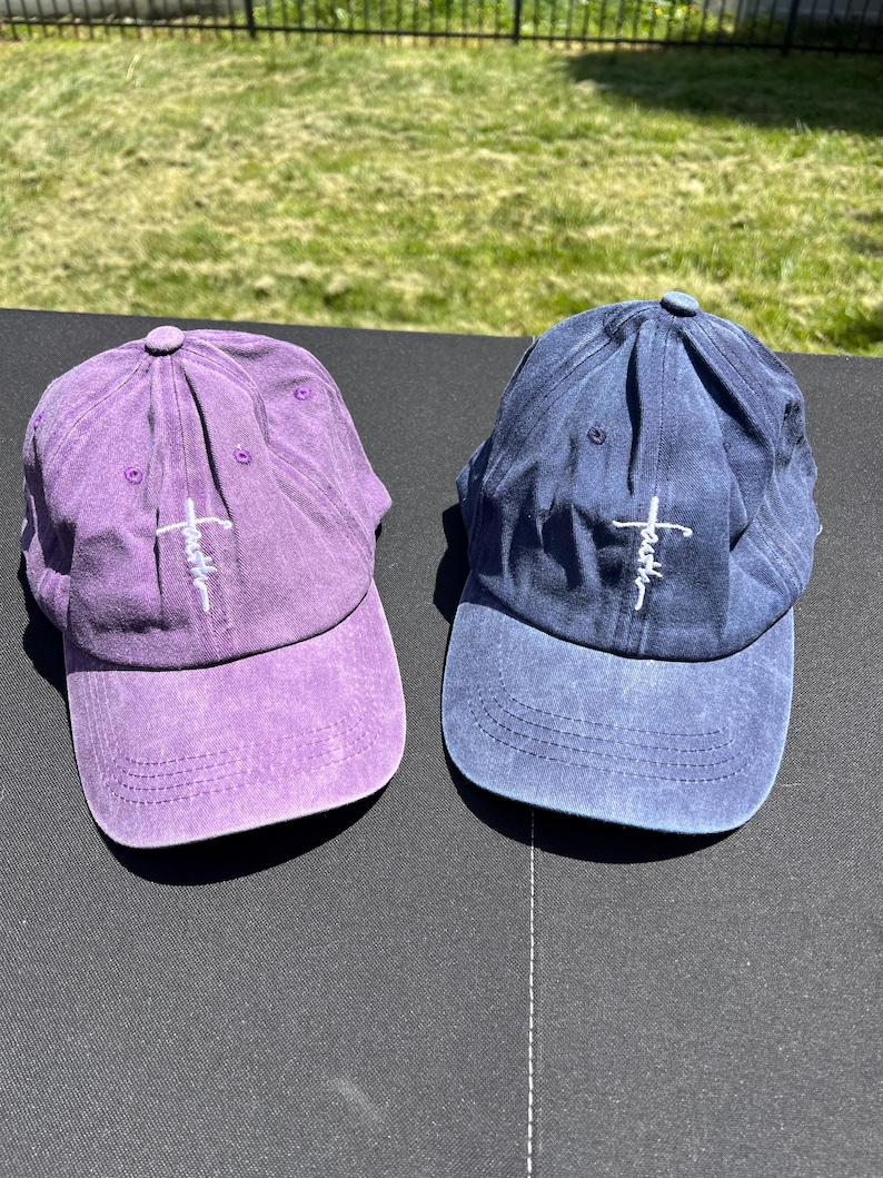 May include: Two baseball caps with a distressed look. One is purple and the other is blue. Both have a white cross with the word "faith" written on it.