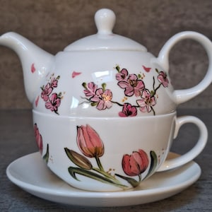May include: A white porcelain tea set with a floral design. The teapot features a pink cherry blossom design and the teacup has a pink tulip design. The set includes a saucer.