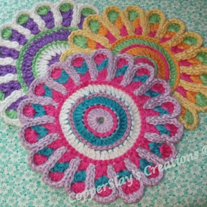 May include: Three crocheted flower-shaped coasters in shades of purple, pink, teal, white, and yellow. The coasters are layered on top of each other, with the largest coaster on the bottom and the smallest coaster on top. The coasters are made with a variety of stitches, including single crochet, double crochet, and treble crochet.