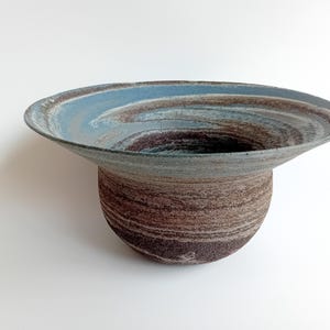 May include: A ceramic bowl with a wide, shallow rim and a rounded base. The bowl is decorated with swirling patterns of blue and brown glaze.