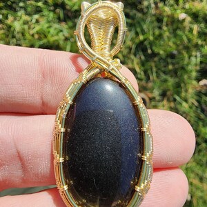 Obsidiana con brillo dorado, envuelta meticulosamente a mano en cobre bañado en oro de 14 k.