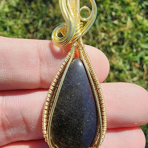 Obsidiana con brillo dorado, envuelta meticulosamente a mano en cobre bañado en oro de 14 k.