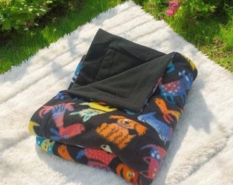 May include: A black fleece blanket with a colorful animal print design. The blanket is folded in half and has a black fleece lining.