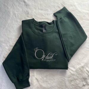 Puede incluir: Una sudadera verde oscuro con el texto "The O dust Ballroom" bordado en blanco en la parte delantera.