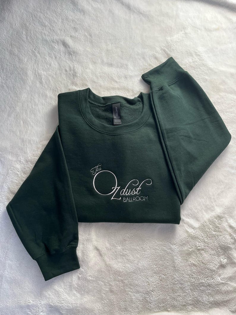 Puede incluir: Una sudadera verde oscuro con el texto "The O dust Ballroom" bordado en blanco en la parte delantera.