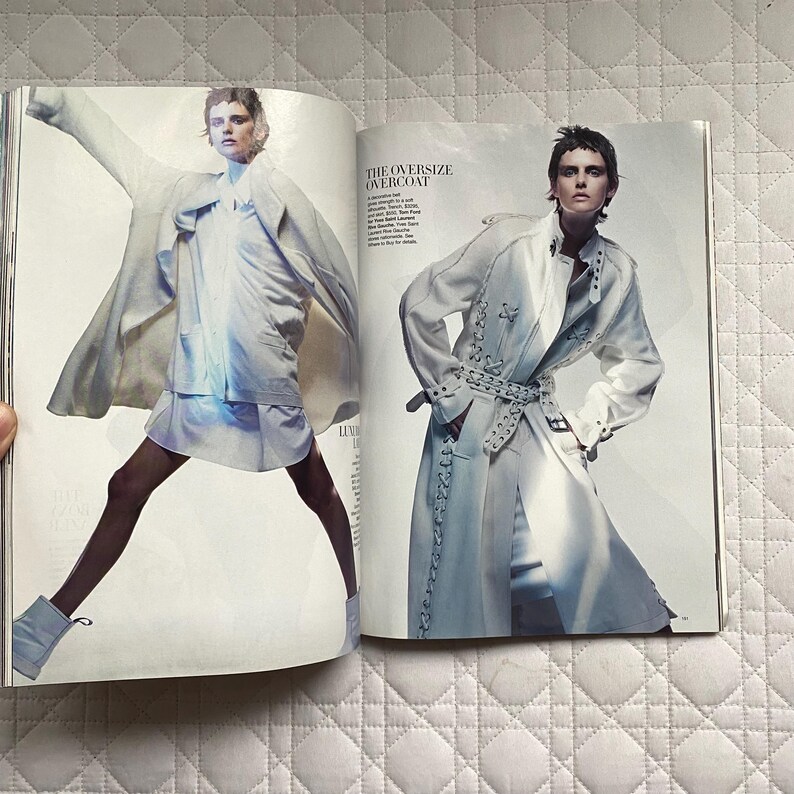 May include: Two models wearing long, white, oversized coats. The model on the left is wearing a white shirt and black tights. The model on the right is wearing a white shirt and white pants. The text "THE OVERSIZE OVERCOAT" is printed on the page.