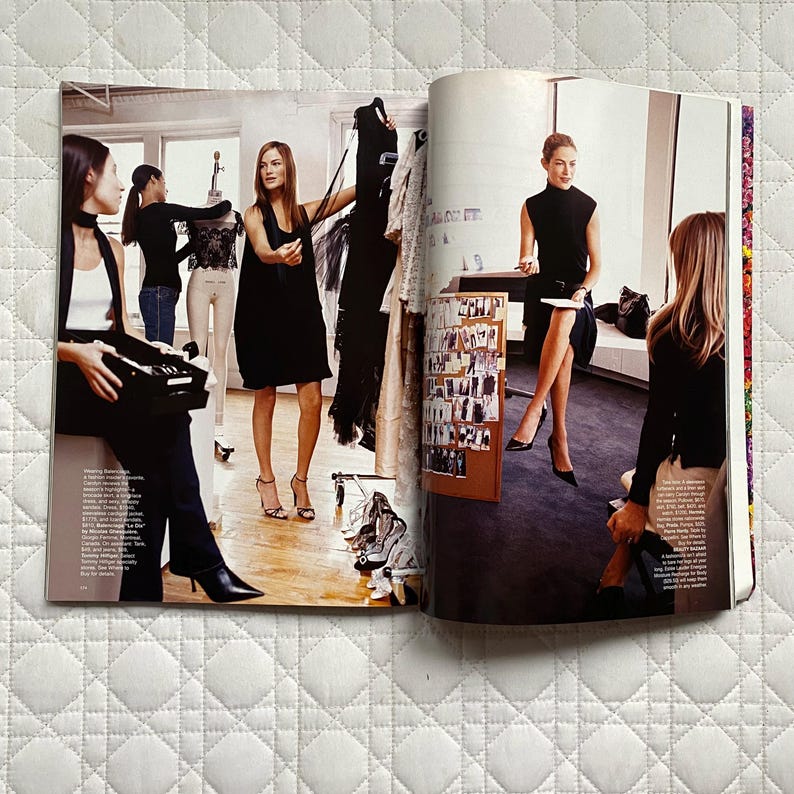 May include: A magazine spread featuring three women in a fashion studio. The women are wearing black clothing and are looking at a rack of clothes. The magazine spread also includes a text box with information about the fashion shoot.