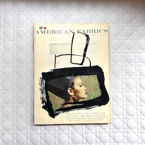Puede incluir: Portada de revista vintage para American Fabrics. La portada presenta a una mujer de perfil con un tocado negro y grandes pendientes de aro dorados. El título de la revista está en negrita, con un diseño de trazo negro.