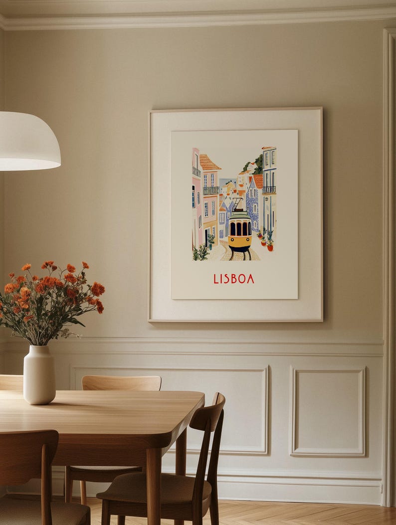 May include: A framed illustration of a street scene in Lisbon, Portugal. The illustration features colorful buildings, a yellow tram, and the word "LISBOA" in red lettering.