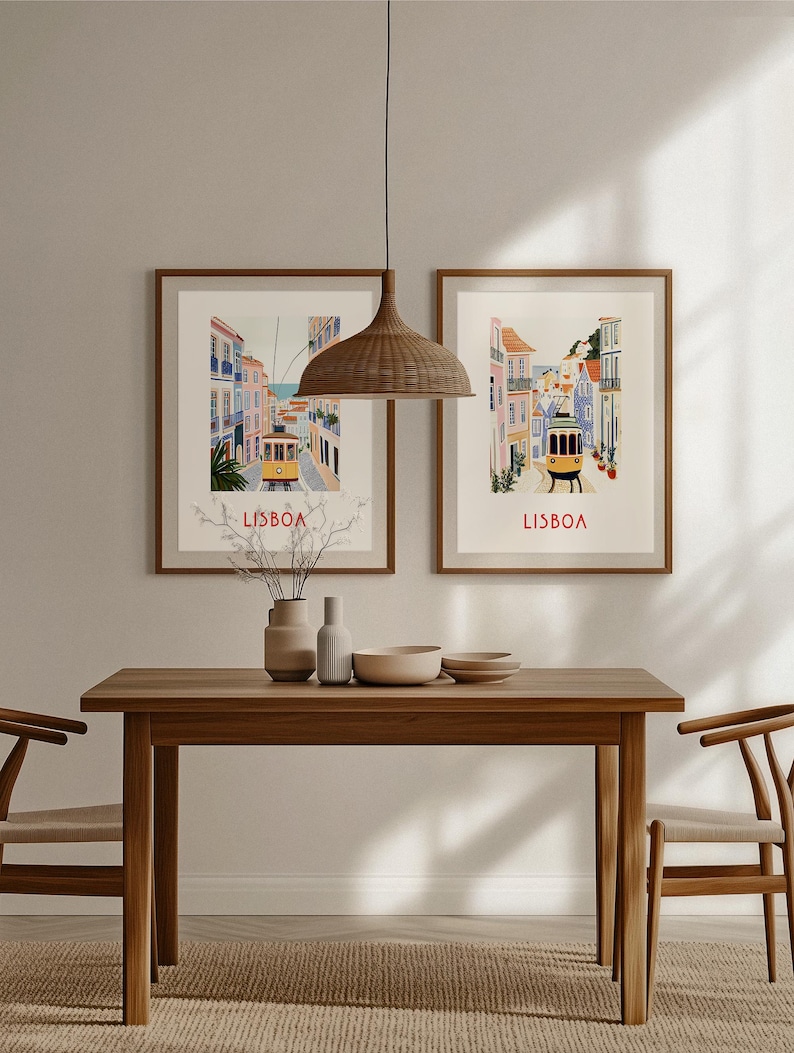 May include: Two framed vintage travel posters with illustrations of Lisbon, Portugal. The posters feature a yellow tram traveling up a hill with colorful buildings on either side. The text "LISBOA" is printed in red at the bottom of each poster.