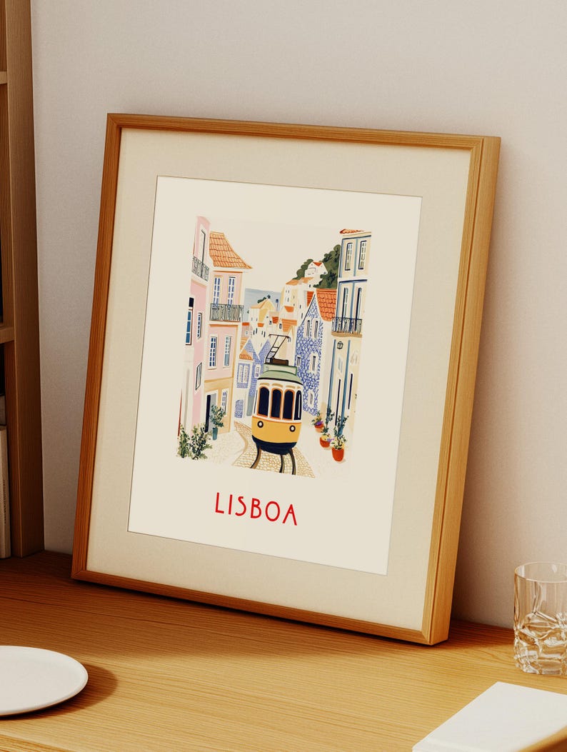 May include: A framed illustration of a yellow tram traveling up a hill in Lisbon, Portugal. The buildings are colorful and the street is cobblestone. The text "LISBOA" is printed in red at the bottom of the image.